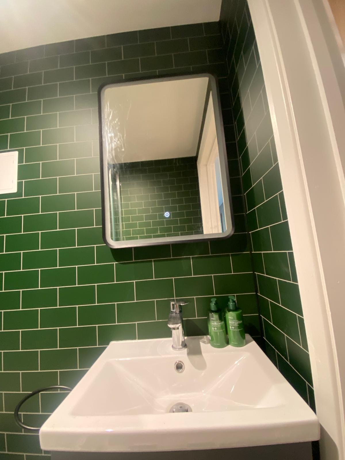 Bathroom with deep green metro tiles, a white basin and a mirror cabinet