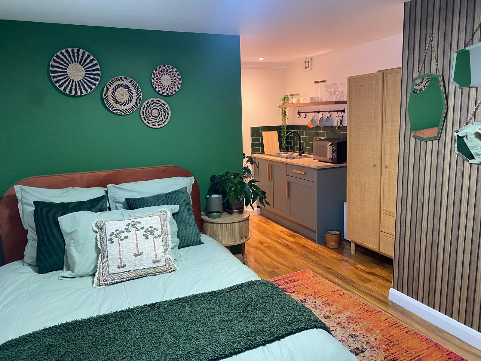 Refurbished room with a deep green feature wall, double bed, kitchenette and wood floor