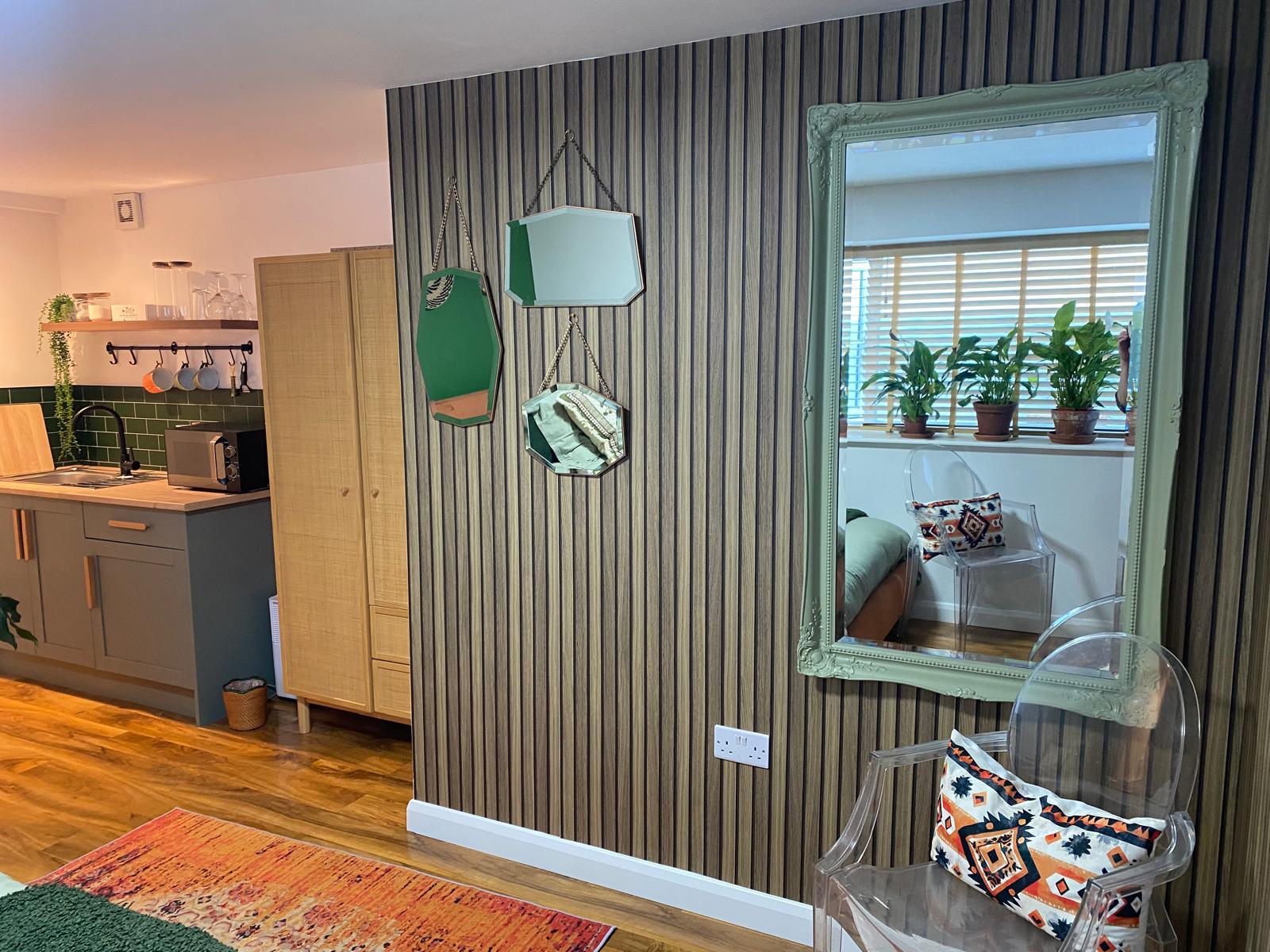 Slatted wood wall panelling with a mirror, and a kitchenette beyond